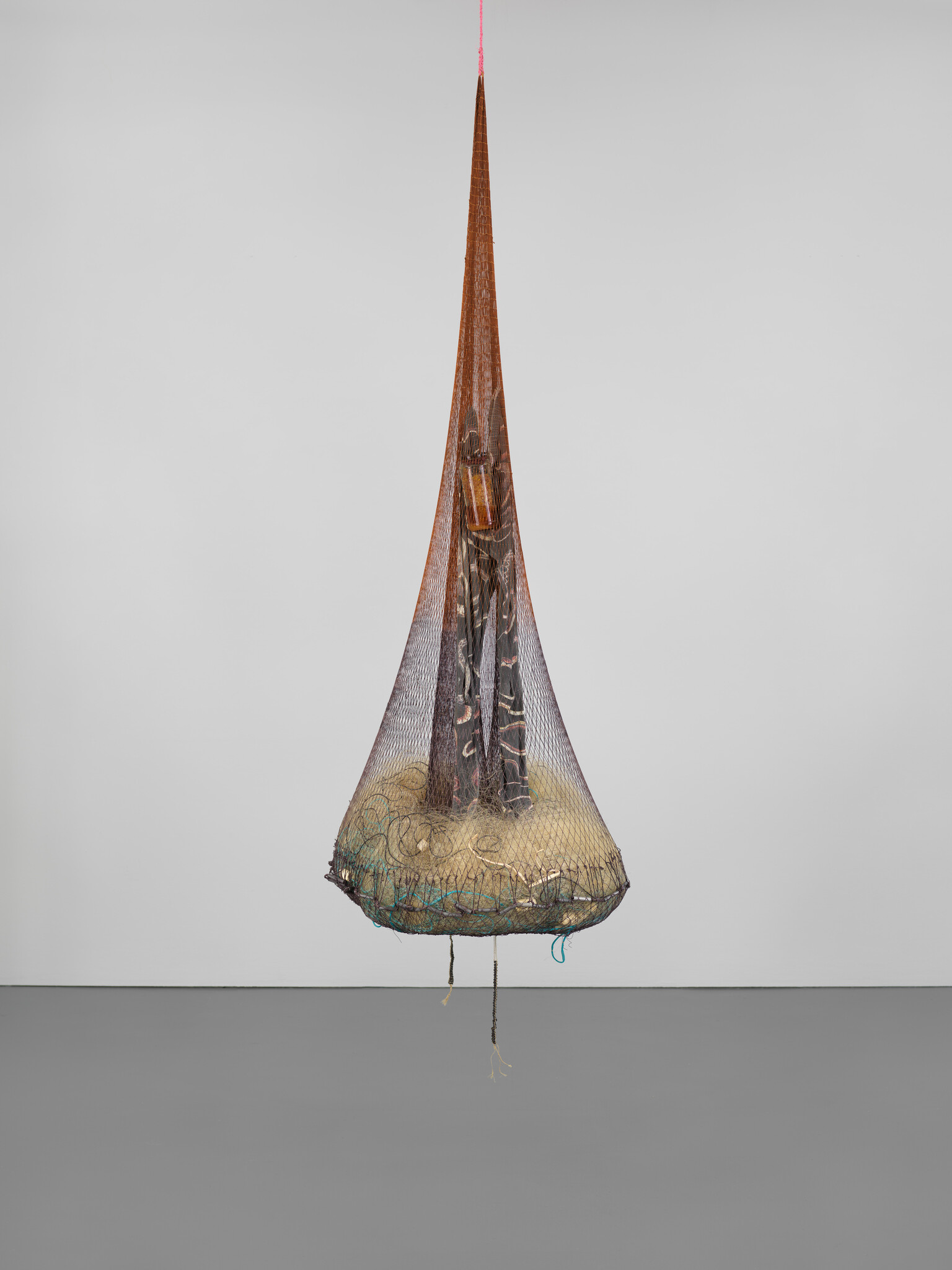 A tall pointed hanging net holds bundled fabric, straw, and ropes suspended above the floor.