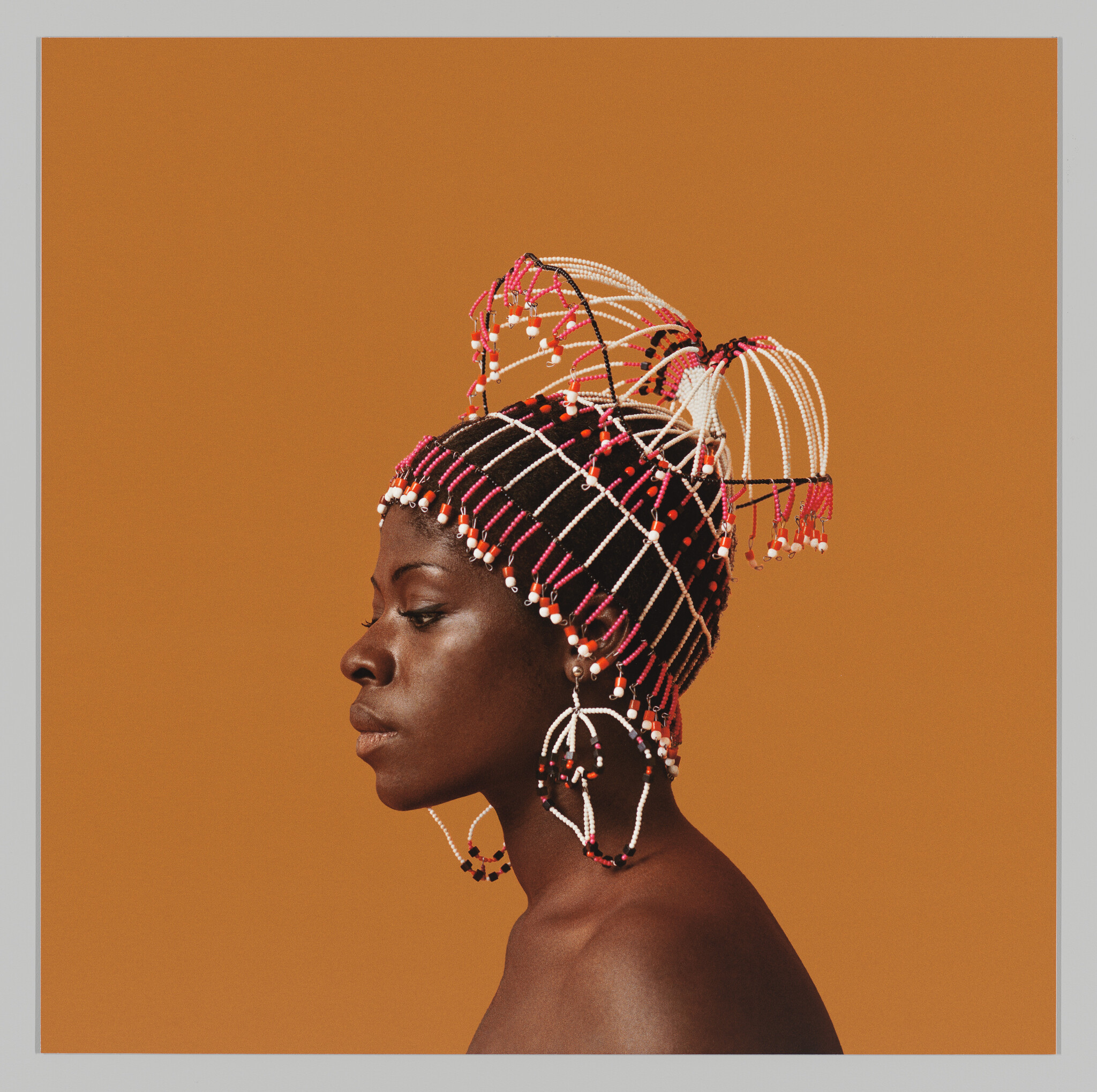 A profile portrait of a woman against an orange background, wearing an elaborate beaded headdress with strands of beads in black, white, and red, and large hoop earrings. Her expression is serene and contemplative.