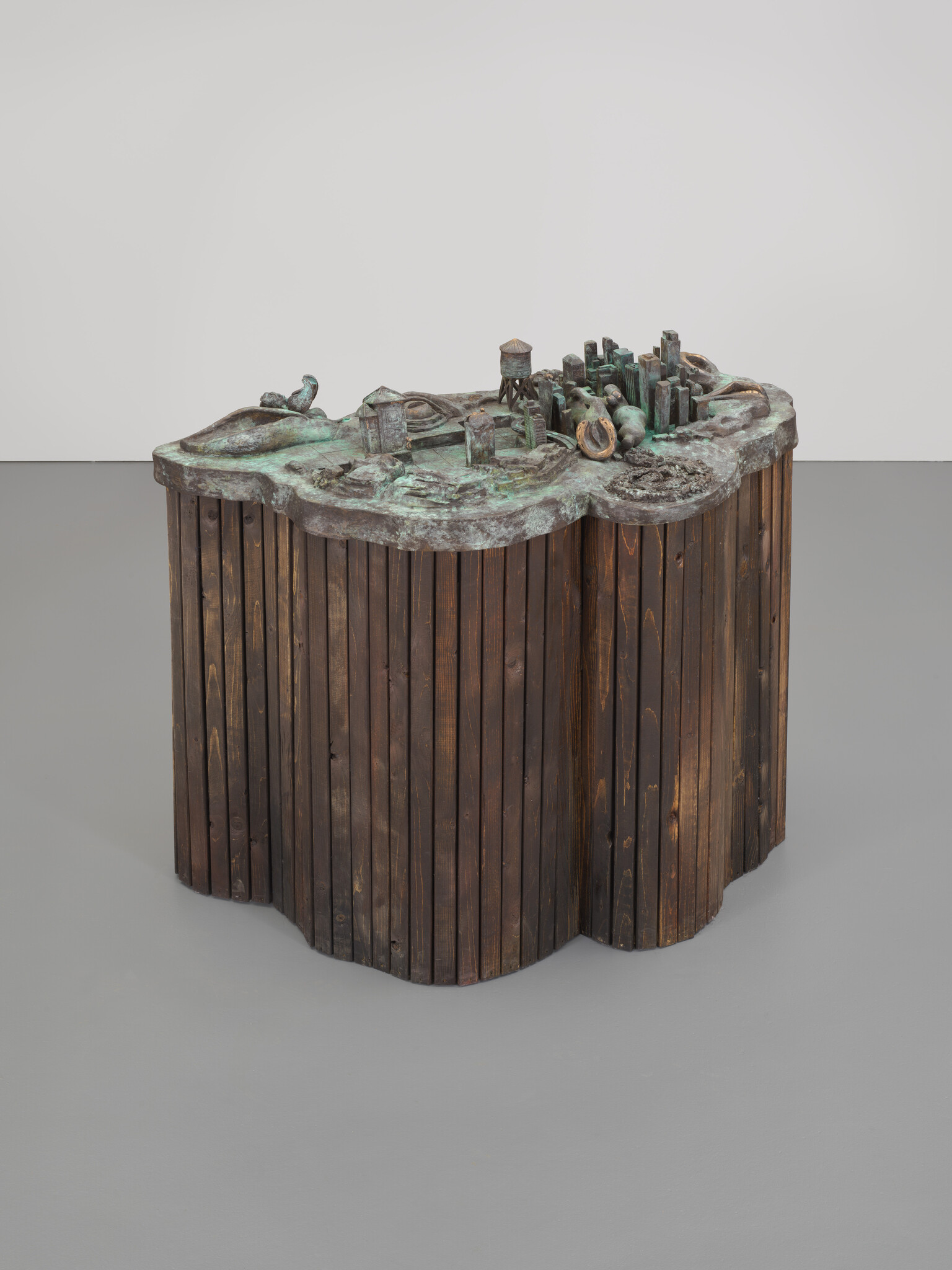 Bronze city model with small buildings and a water tower mounted on a curved wooden base.