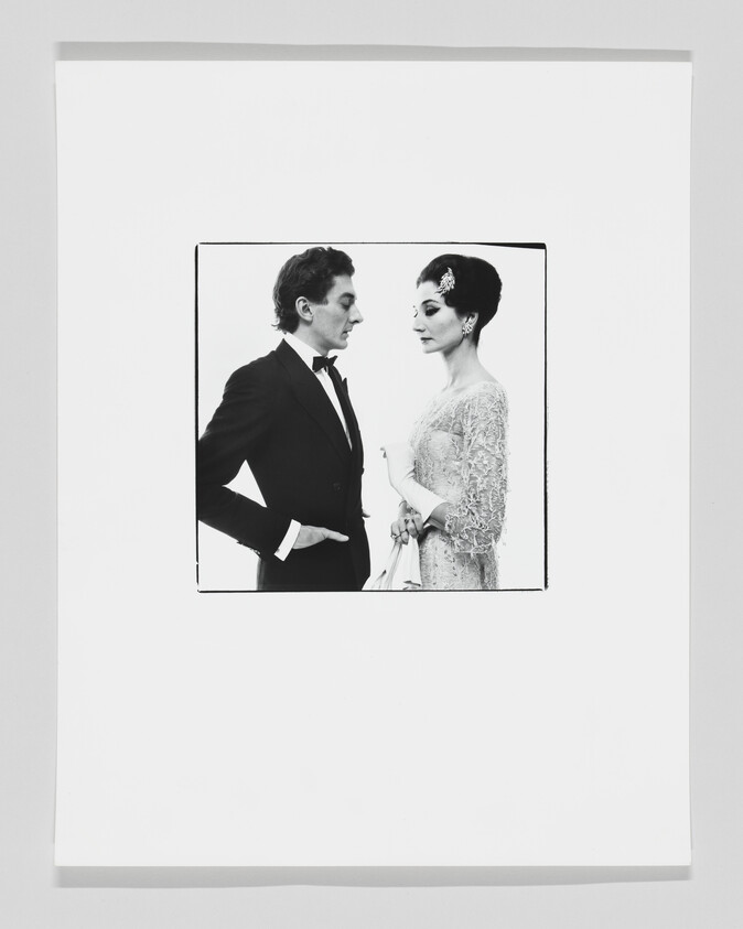 A man in a tuxedo and a woman in an elegant dress face each other in a formal pose.