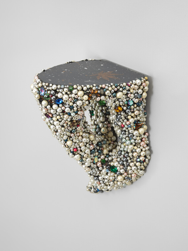 Small wall shelf covered in clusters of pearls and colorful beads, creating a textured, decorative surface.