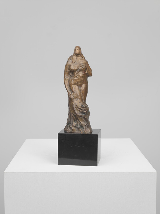 Bronze sculpture of a standing woman with draped clothing on a black pedestal atop a white plinth.