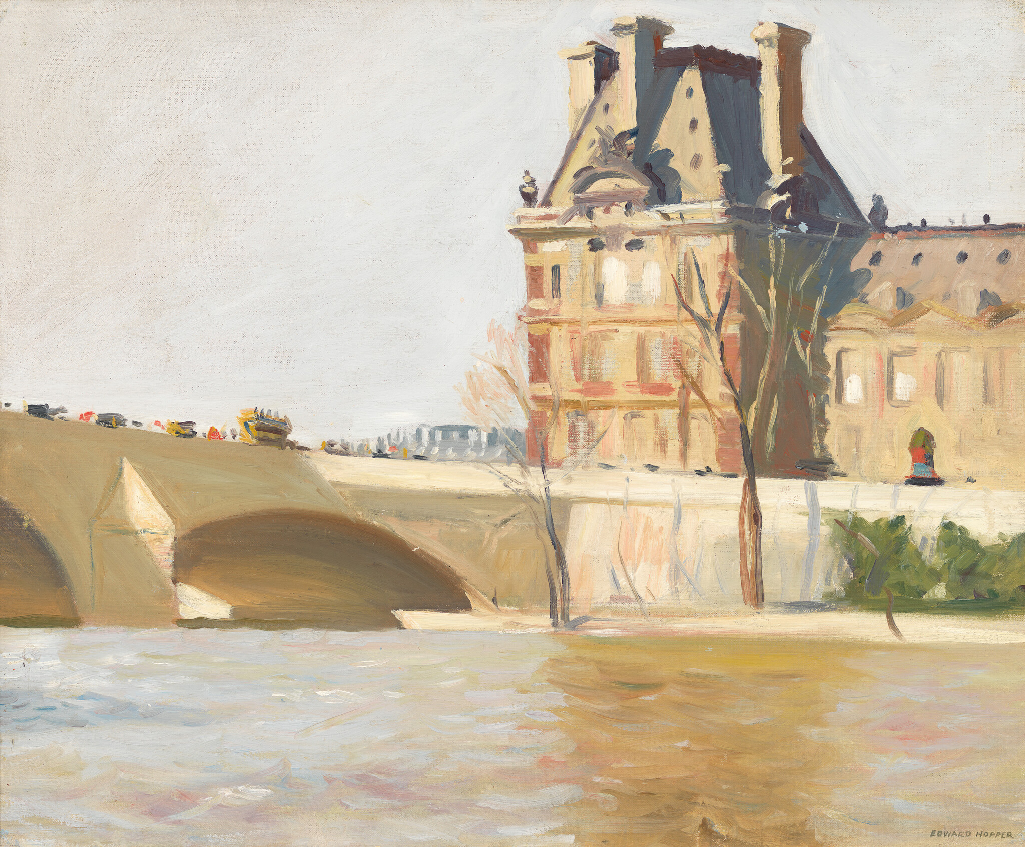 A sunlit stone bridge crosses a calm river beside a tall historic building with bare trees.