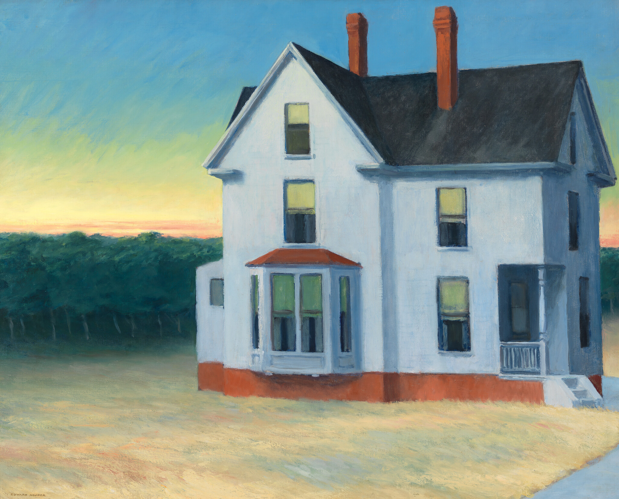 A large white two-story house stands alone near fields at sunset with lit windows.