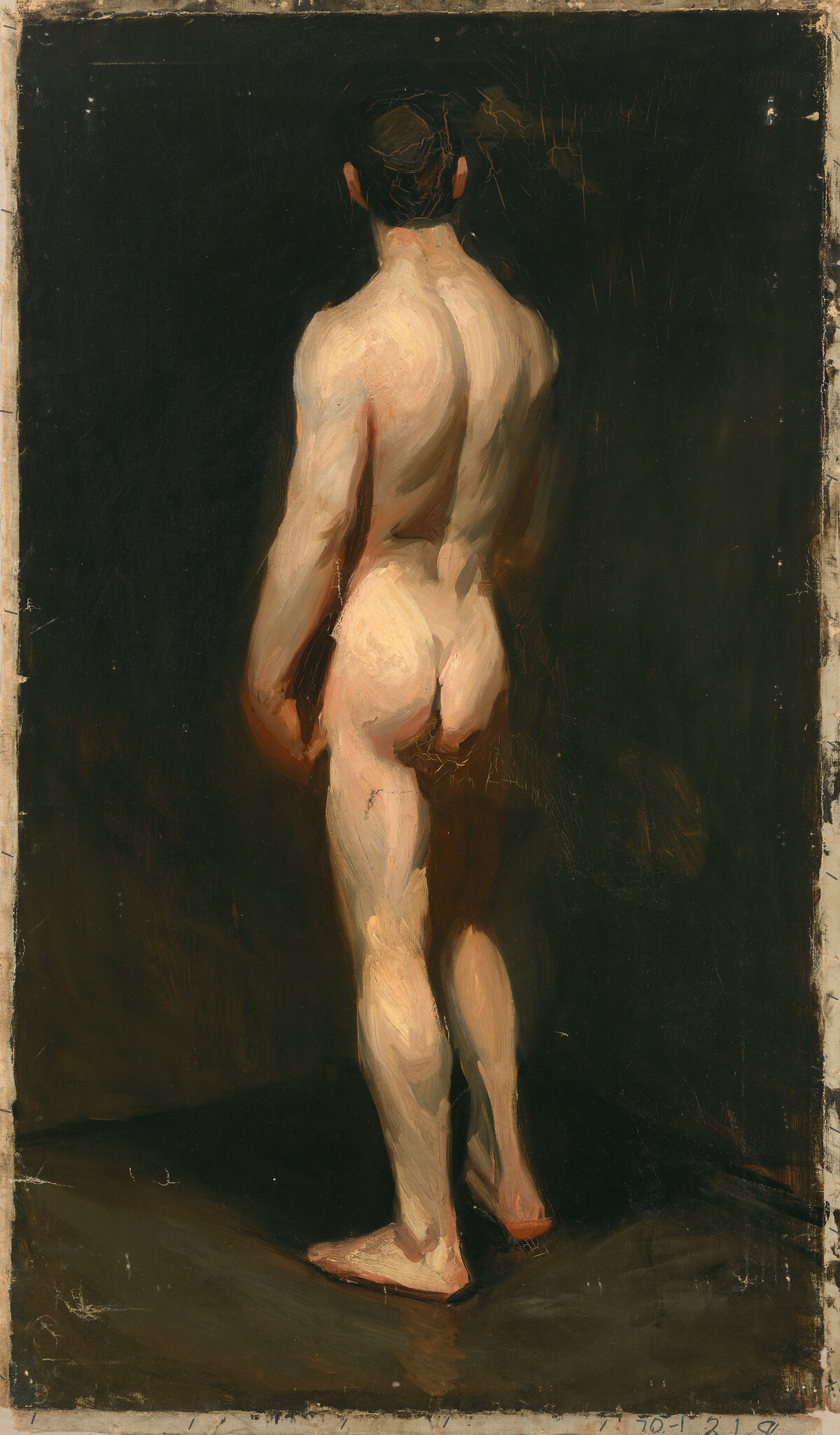 Naked man standing with his back to the viewer in a dimly lit studio.