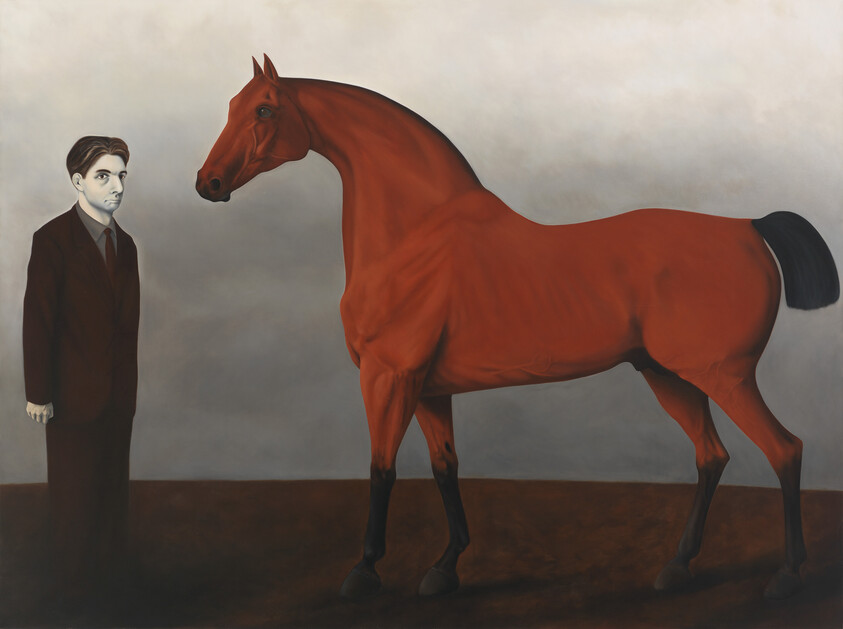 A suited man stands beside a large chestnut horse against a muted gray background.