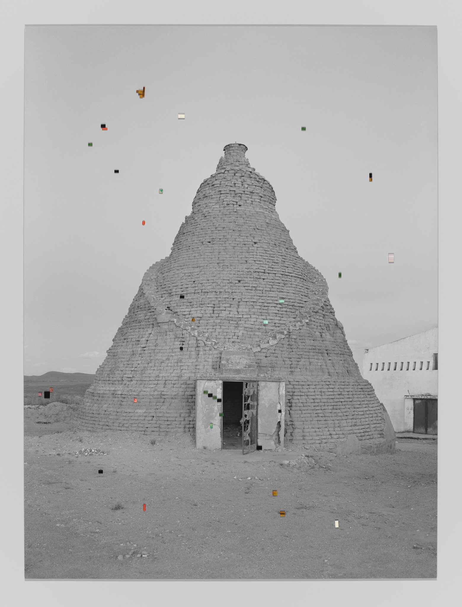 A black-and-white photograph of a large, conical grain silo is adorned by small, colorful precious gems