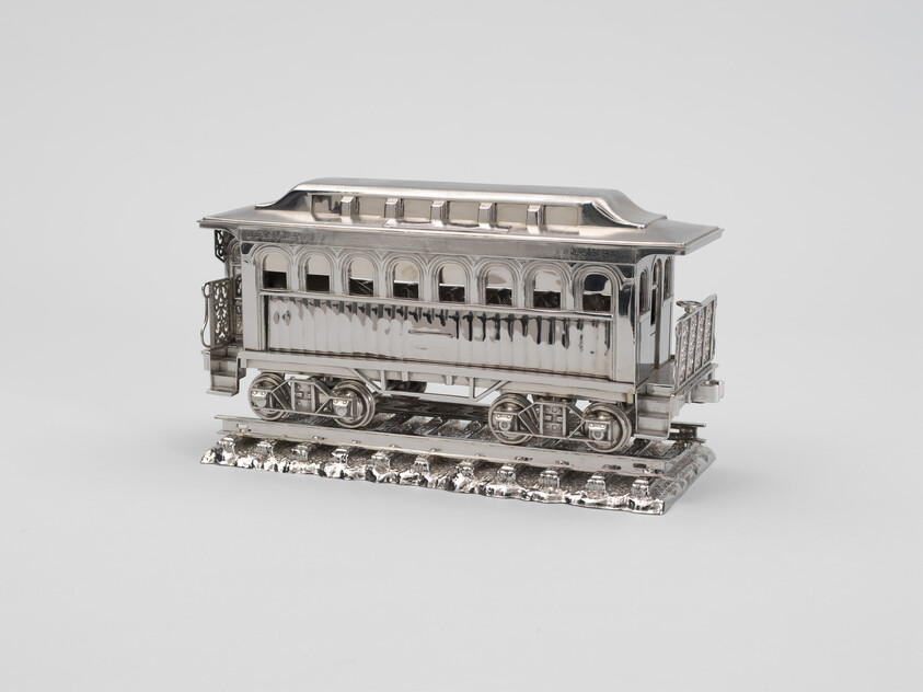 A shiny silver model of a vintage train car sits on a small section of detailed train tracks.