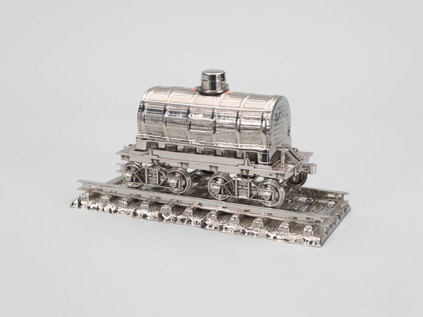 A shiny silver model of a train tank car sits on a short section of metal railroad track.