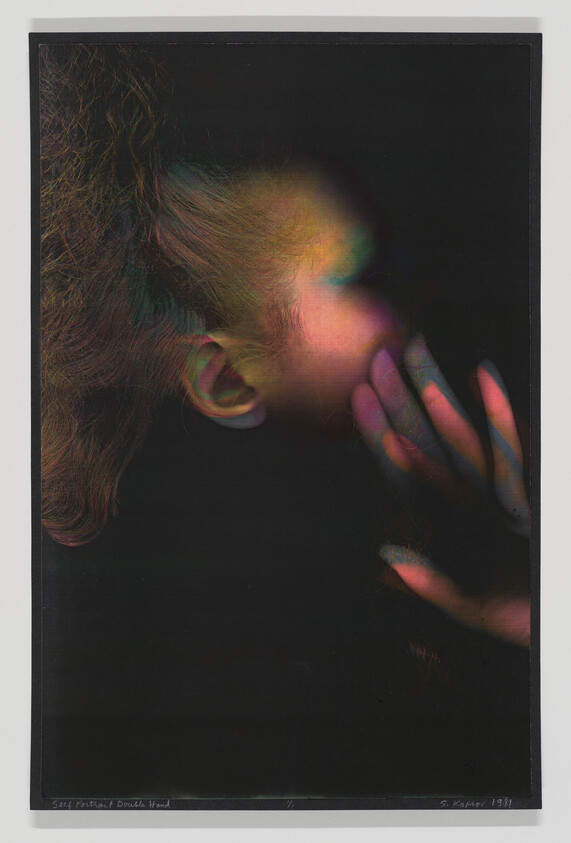 Young person in side profile touches their cheek with hand under colored, blurred lighting.