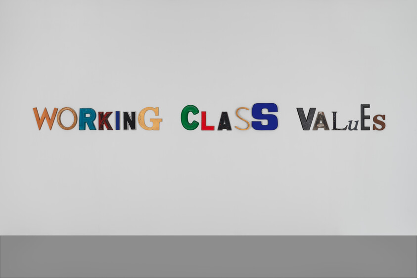 Colorful cutout letters arranged on a white wall spell "Working Class Values" across the center.