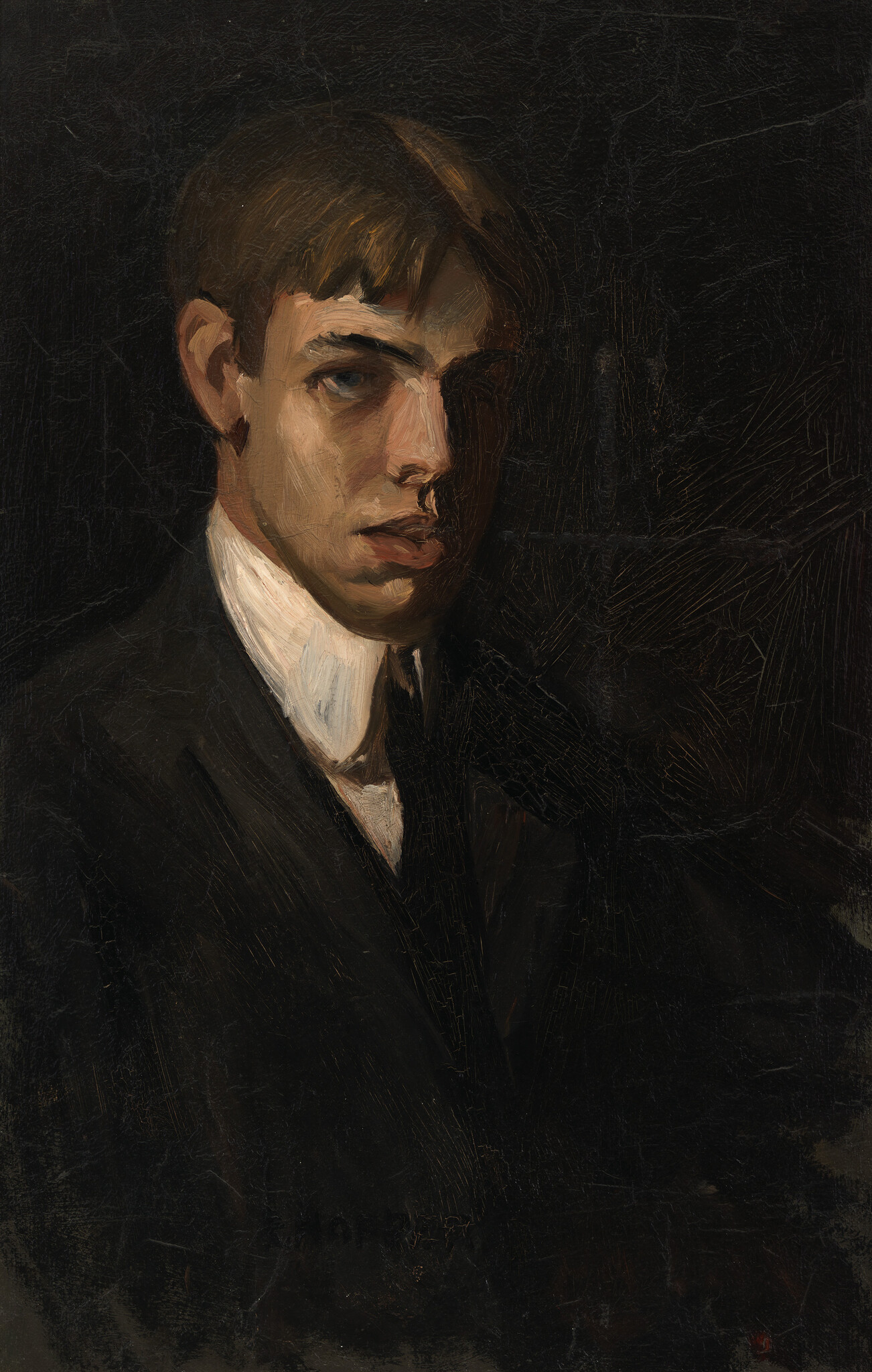 Young man in a dark suit and white collar looking toward the viewer with dramatic lighting.