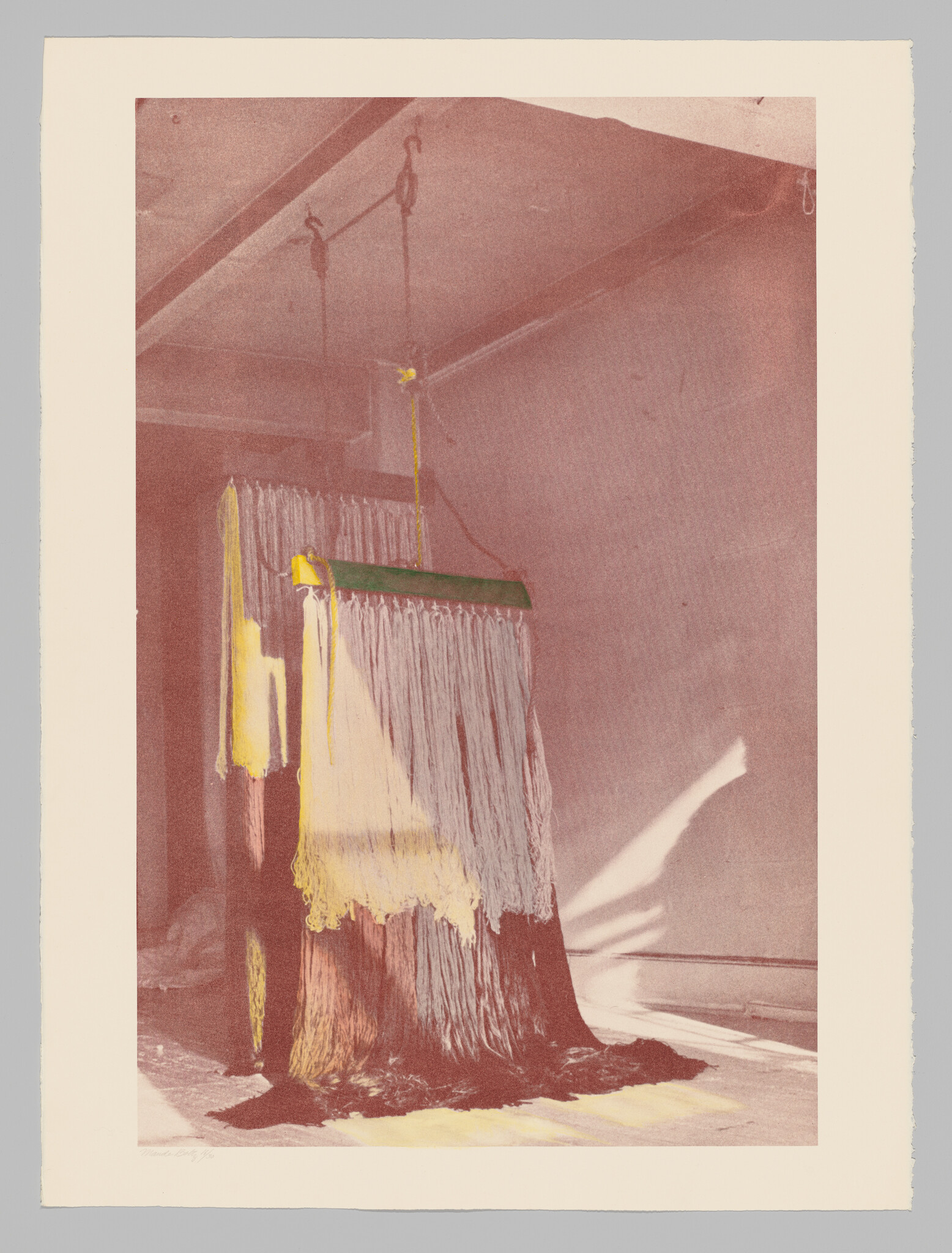 A photograph of an abstract art installation featuring a large rectangular block draped with thick, paint-like material in shades of yellow and white, suspended from the ceiling by chains in an empty room with a shadow cast on the wall.