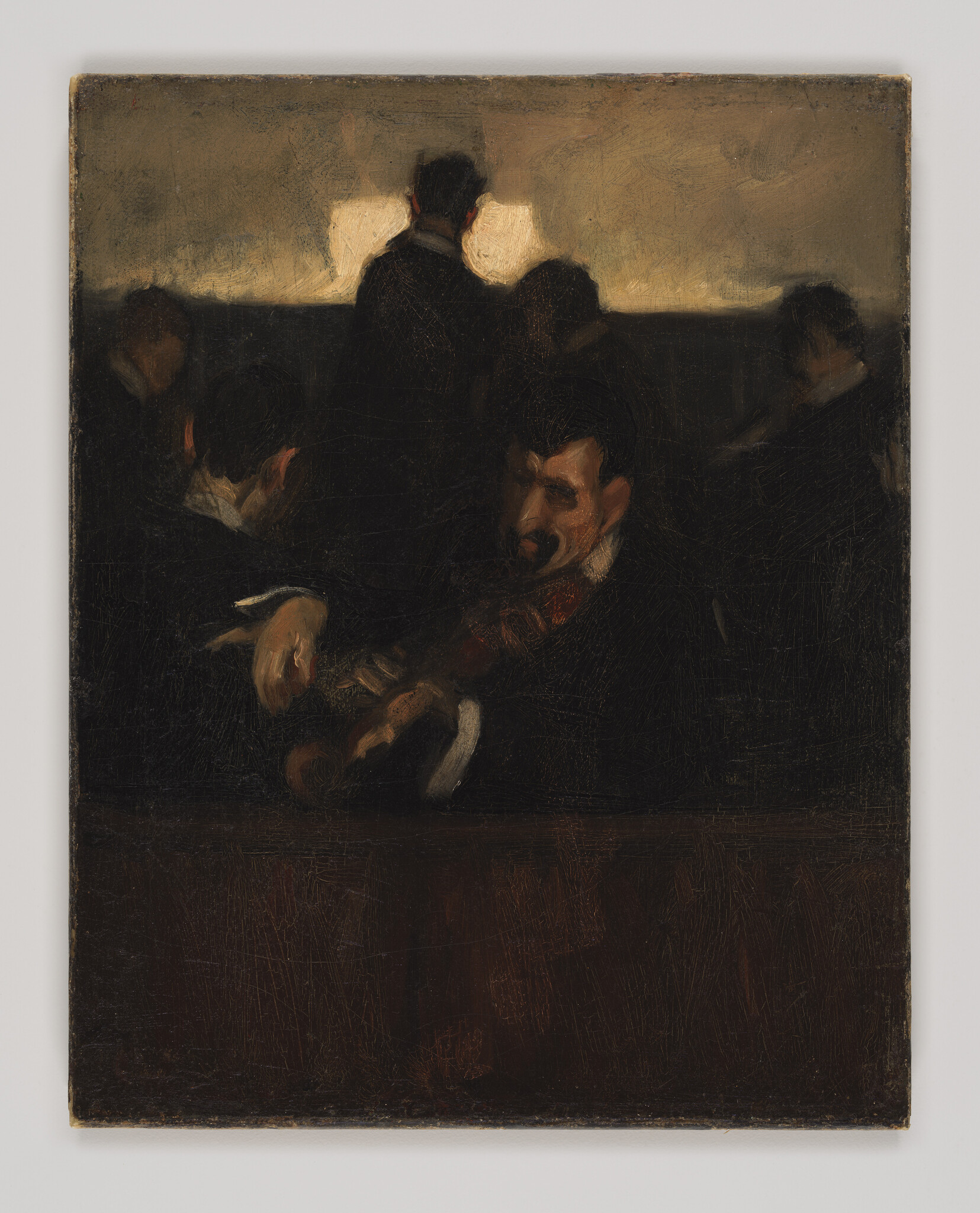 A seated violinist plays in a dimly lit room while others listen in shadow.
