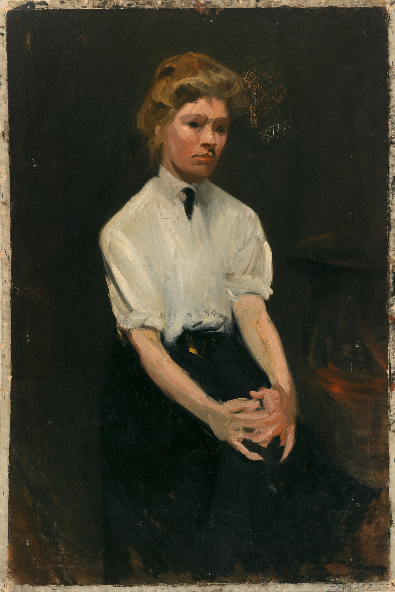 Young woman in white blouse and dark skirt stands with hands clasped and a pensive expression.