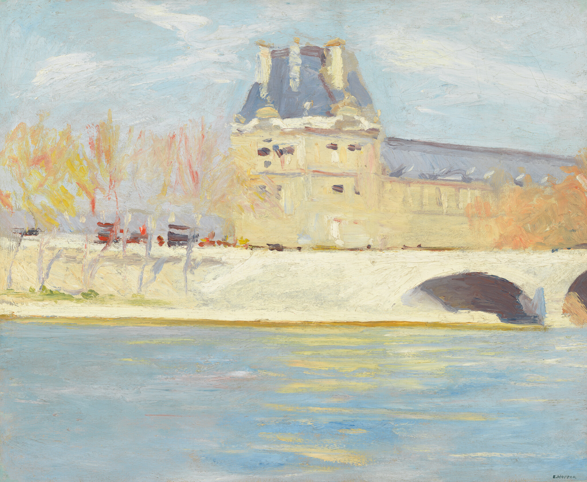 A pale stone bridge with arches crosses a river beside a light-colored building and autumn trees.