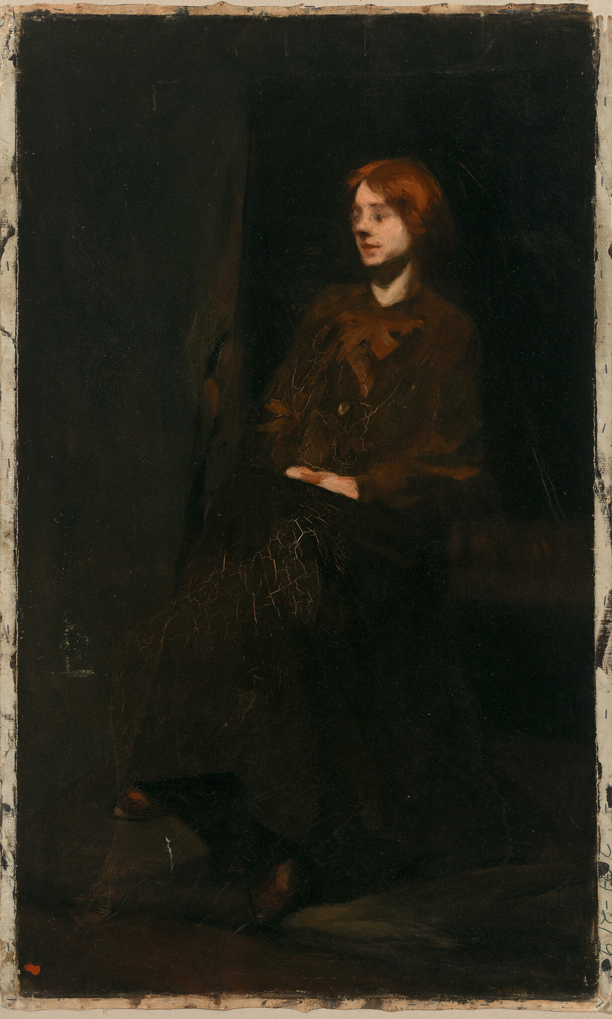 A red-haired woman sits with clasped hands wearing a dark dress against a black background.