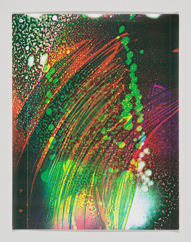 Bright multicolored paint streaks and splatters sweep across a paper background in abstract patterns.