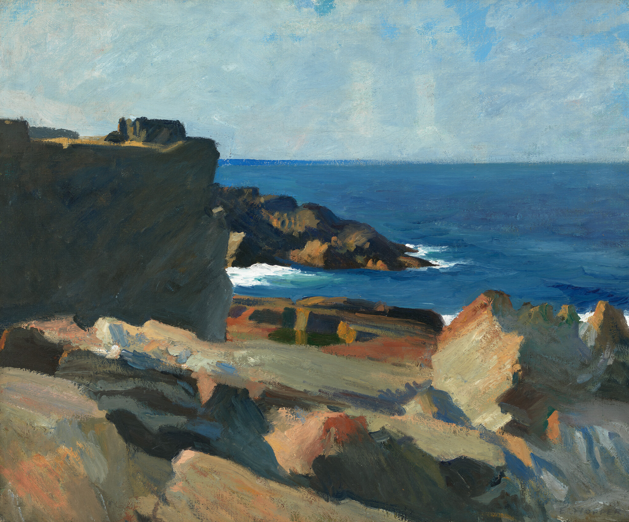 Rocky coastal cliffs overlook deep blue ocean with waves breaking against distant rocks.