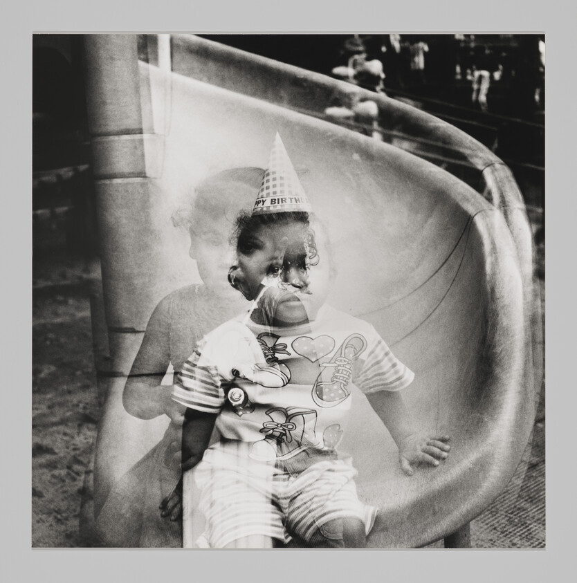 A young child wearing a party hat sits on a playground slide with a double-exposure effect.