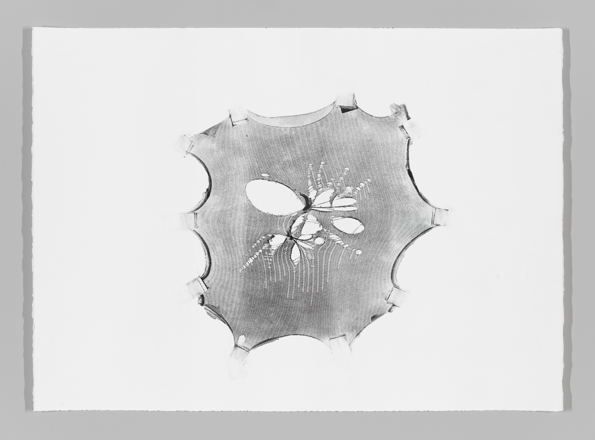 A circular stretched fabric sample with leaf-shaped cutouts pinned at eight points on paper.