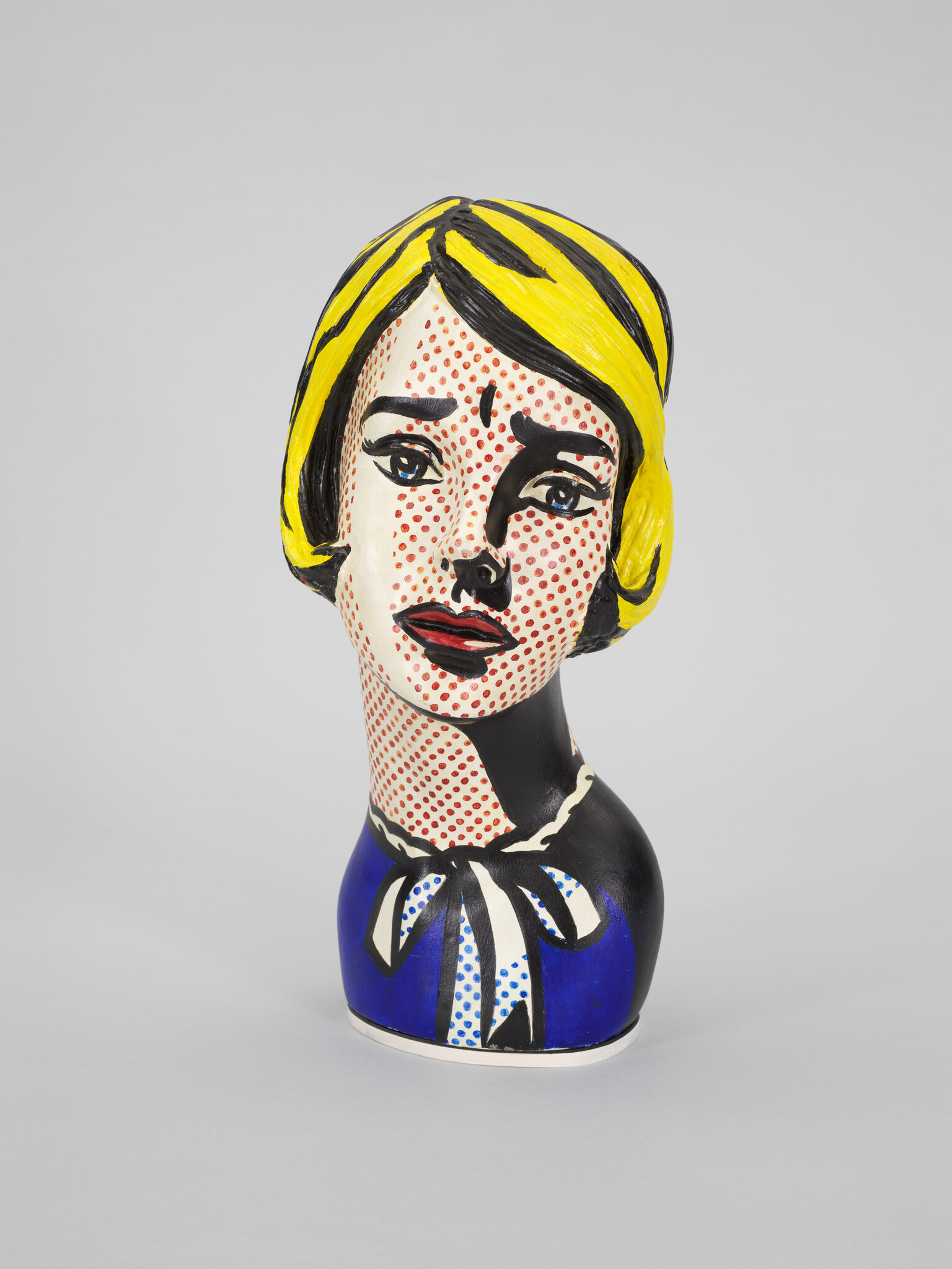 Ceramic pop-art bust of a woman with yellow hair, red dot pattern, and blue bow.