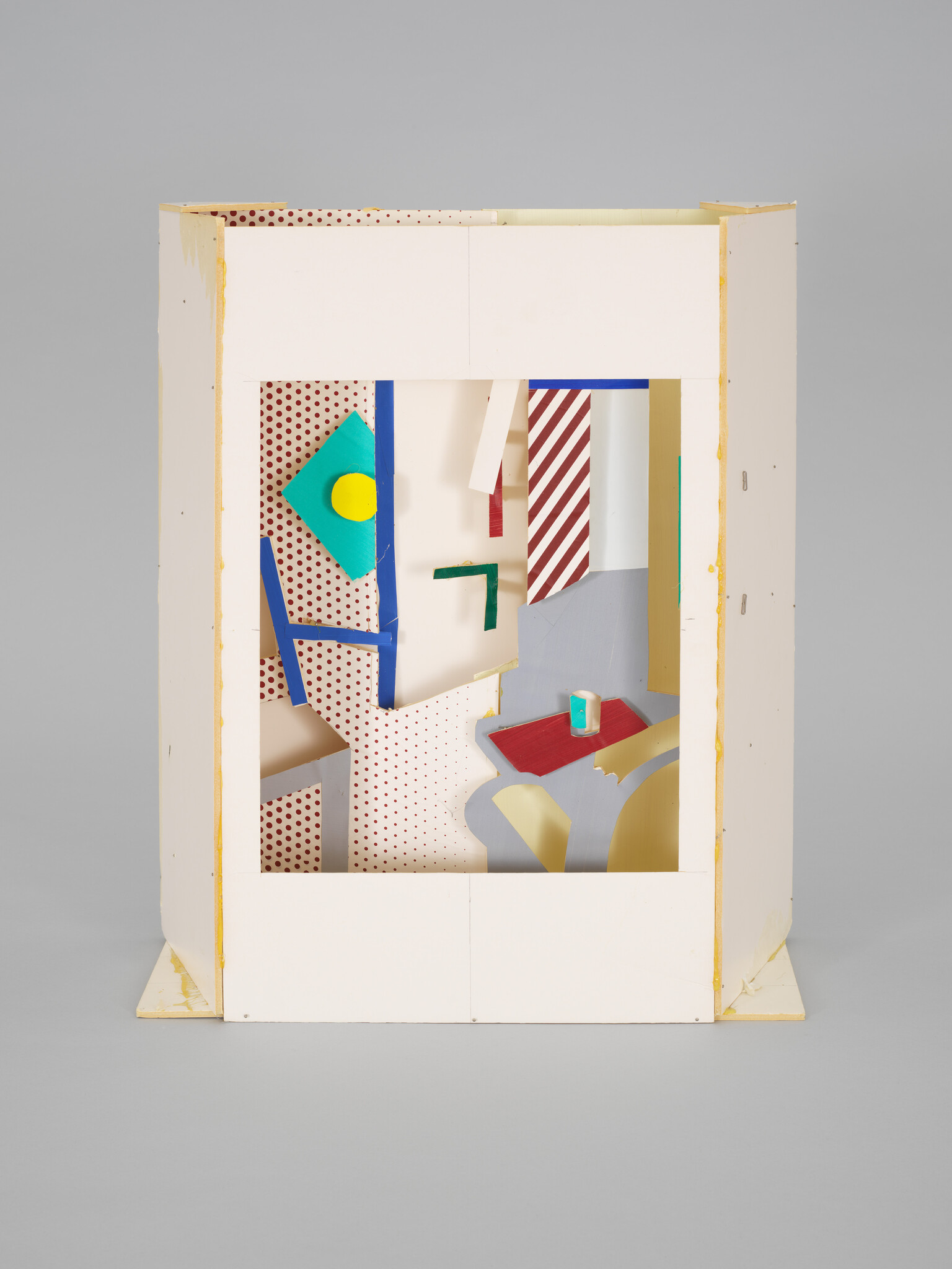 A white box sculpture reveals colorful geometric panels, polka dots, and striped shapes inside.