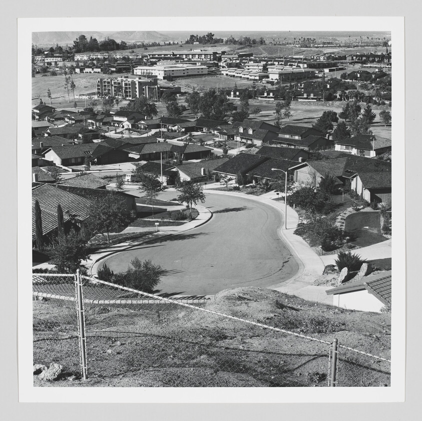 A quiet suburban cul-de-sac lined with single-story houses seen from a fenced hilltop.