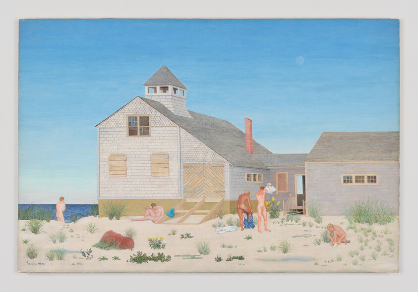 People relax and interact near a beach house on a sunny day, surrounded by sand and grass.