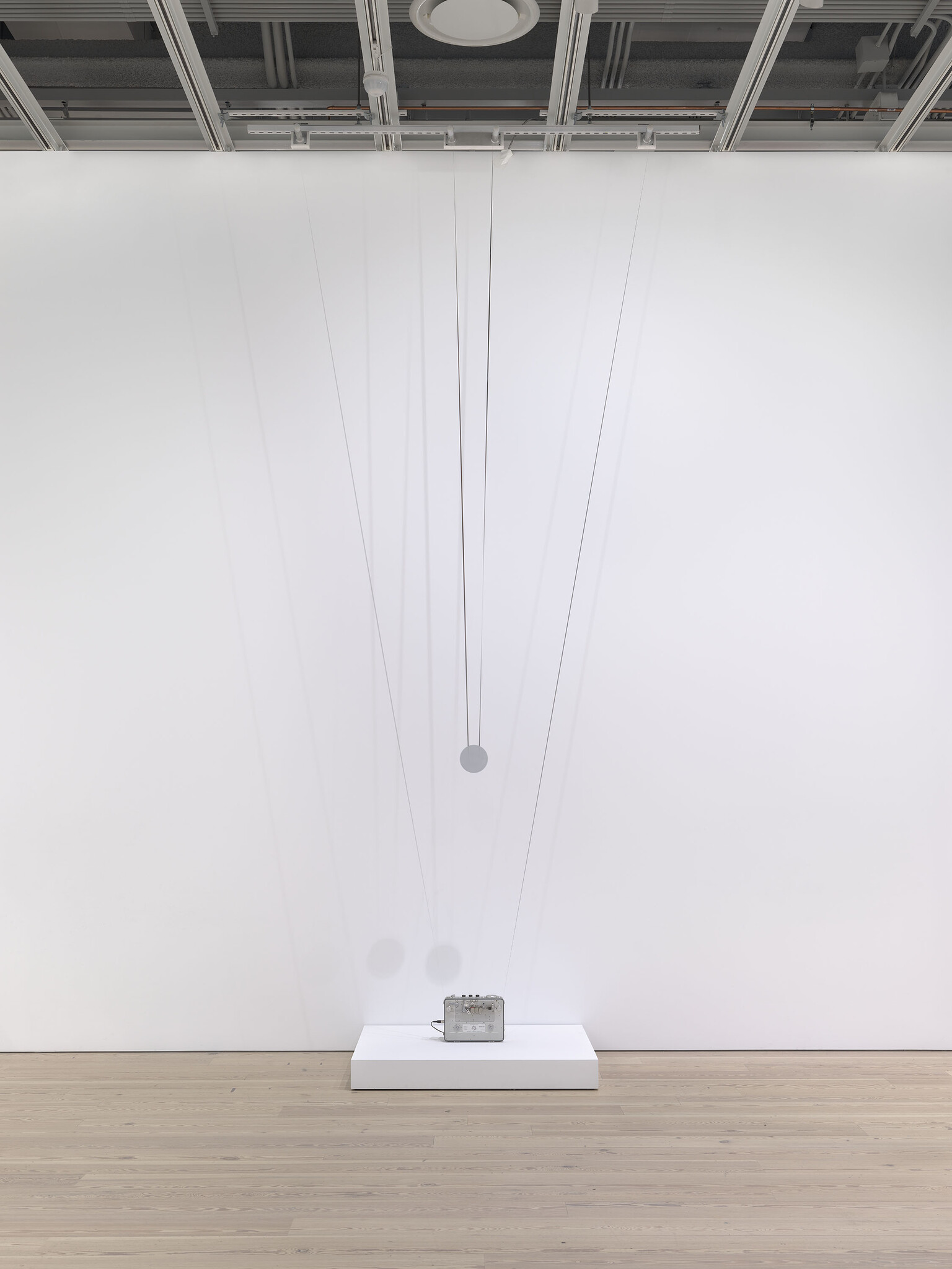 A small metal box sits on a white platform with several thin wires and round weights hanging above it.