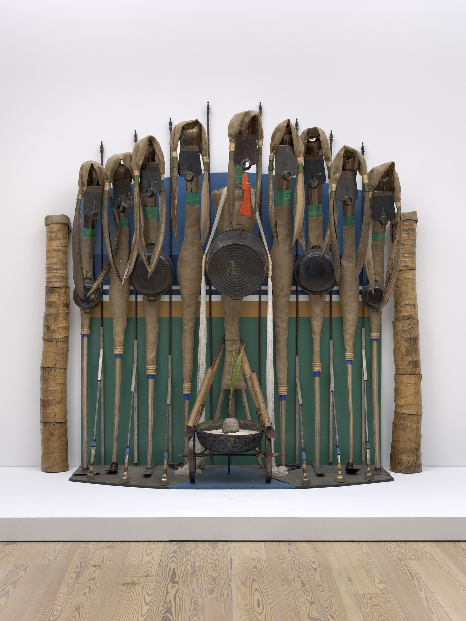 A ceremonial display of paddles, shields, and drums arranged upright against a painted backdrop.