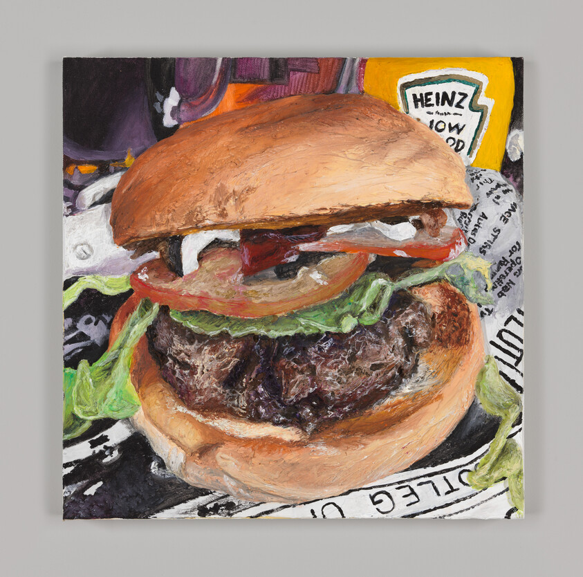 A messy burger topped with lettuce and tomato and sitting beside a bottle of Heinz mustard.