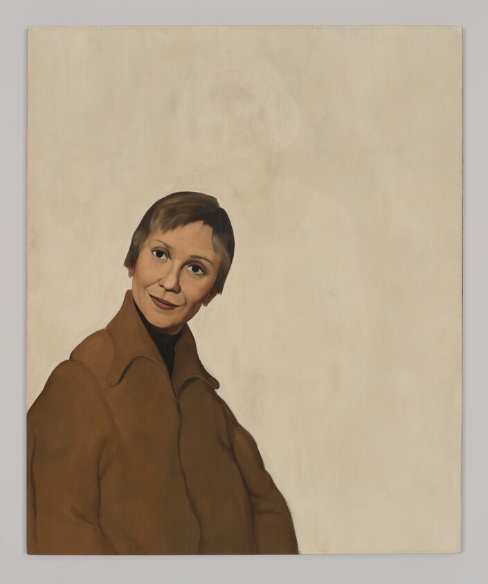 A woman in a brown coat smiles gently and looks slightly to her left.