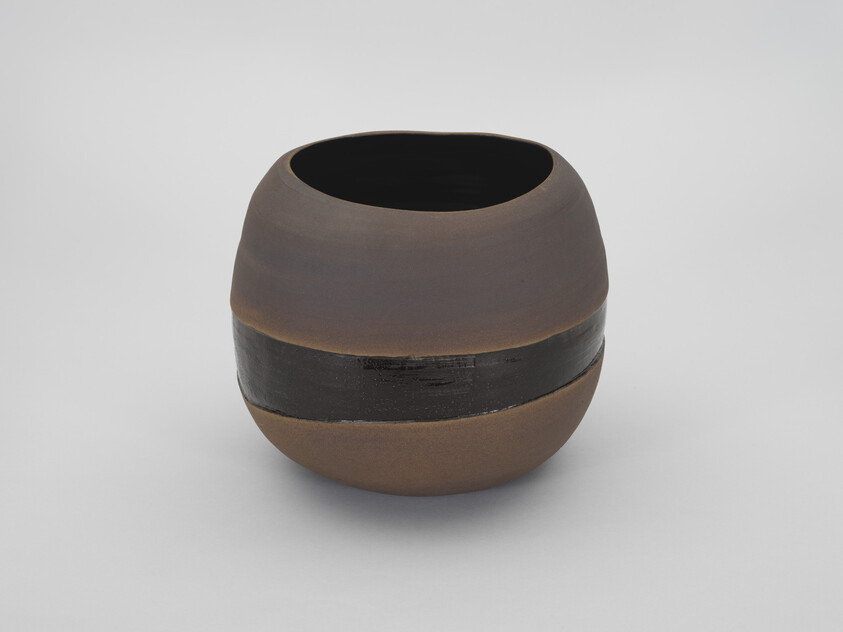 A round brown ceramic pot with a wide glossy black band around its middle.