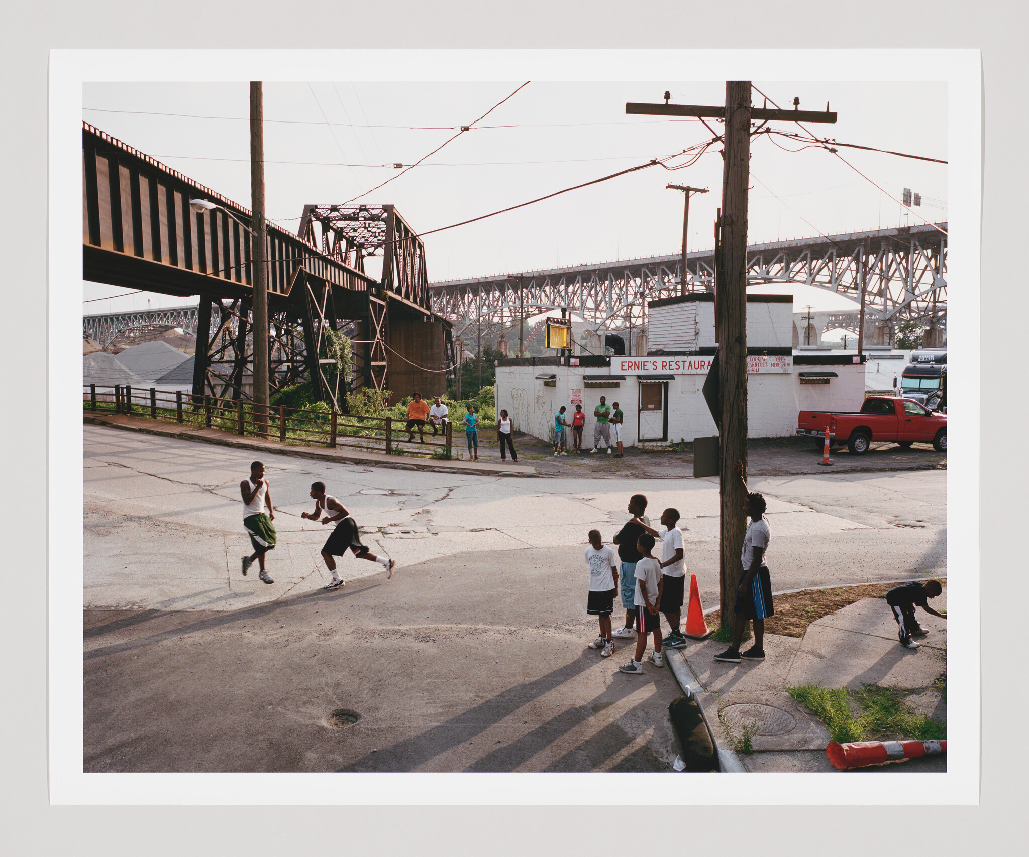 A group of children watch as two boys play and chase a basketball on a cracked street.