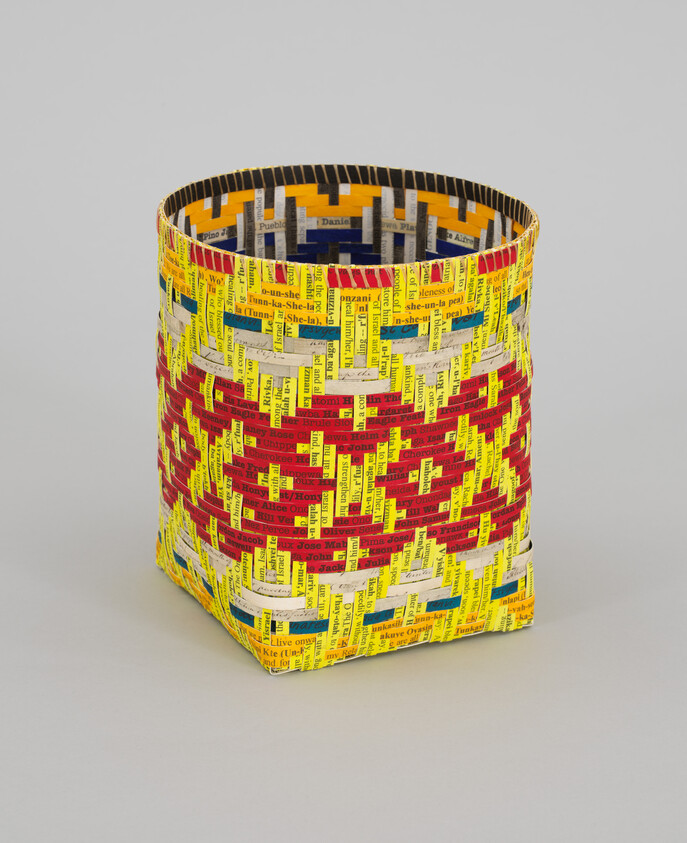 A colorful woven rectangular basket made from printed paper strips with red and yellow geometric patterns.