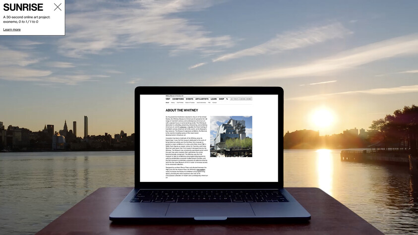 Laptop displaying a webpage about the Whitney Museum, set against a sunrise over a city skyline and river.