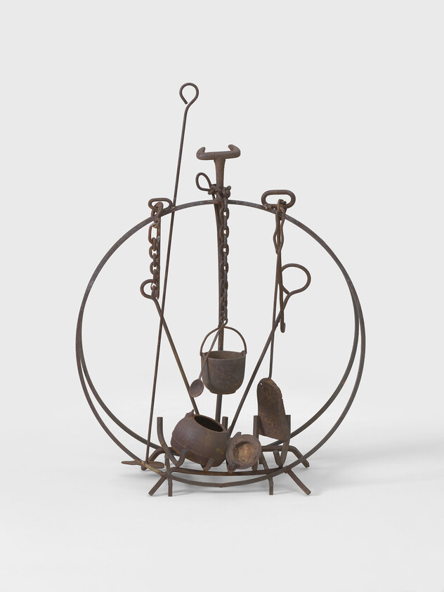 Metal sculpture with circular frame, featuring various hanging and attached tools and objects.