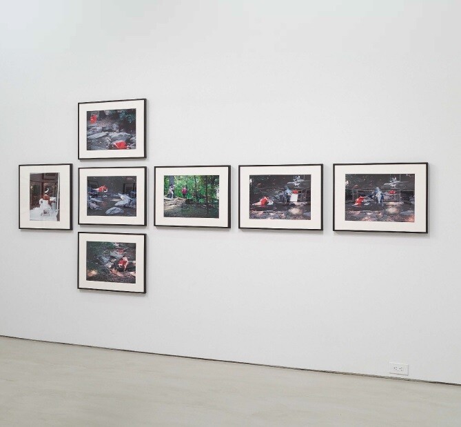 Seven framed photographs are arranged on a white wall, showing people outdoors, some wearing red clothing.