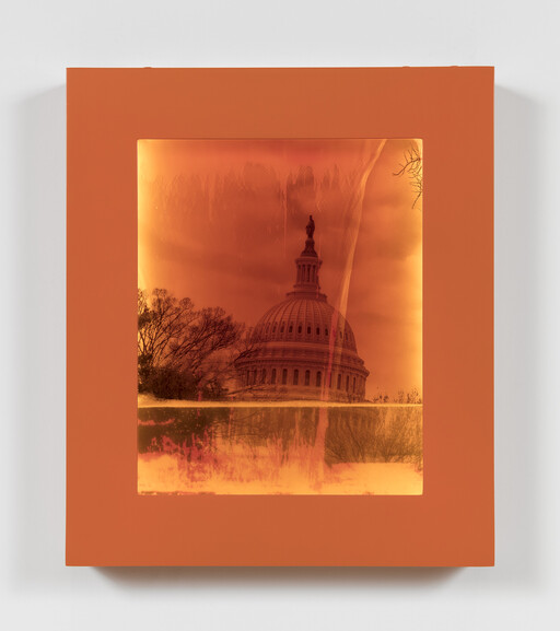 The U.S. Capitol dome appears reflected inside an orange framed artwork with warm, glowing tones.