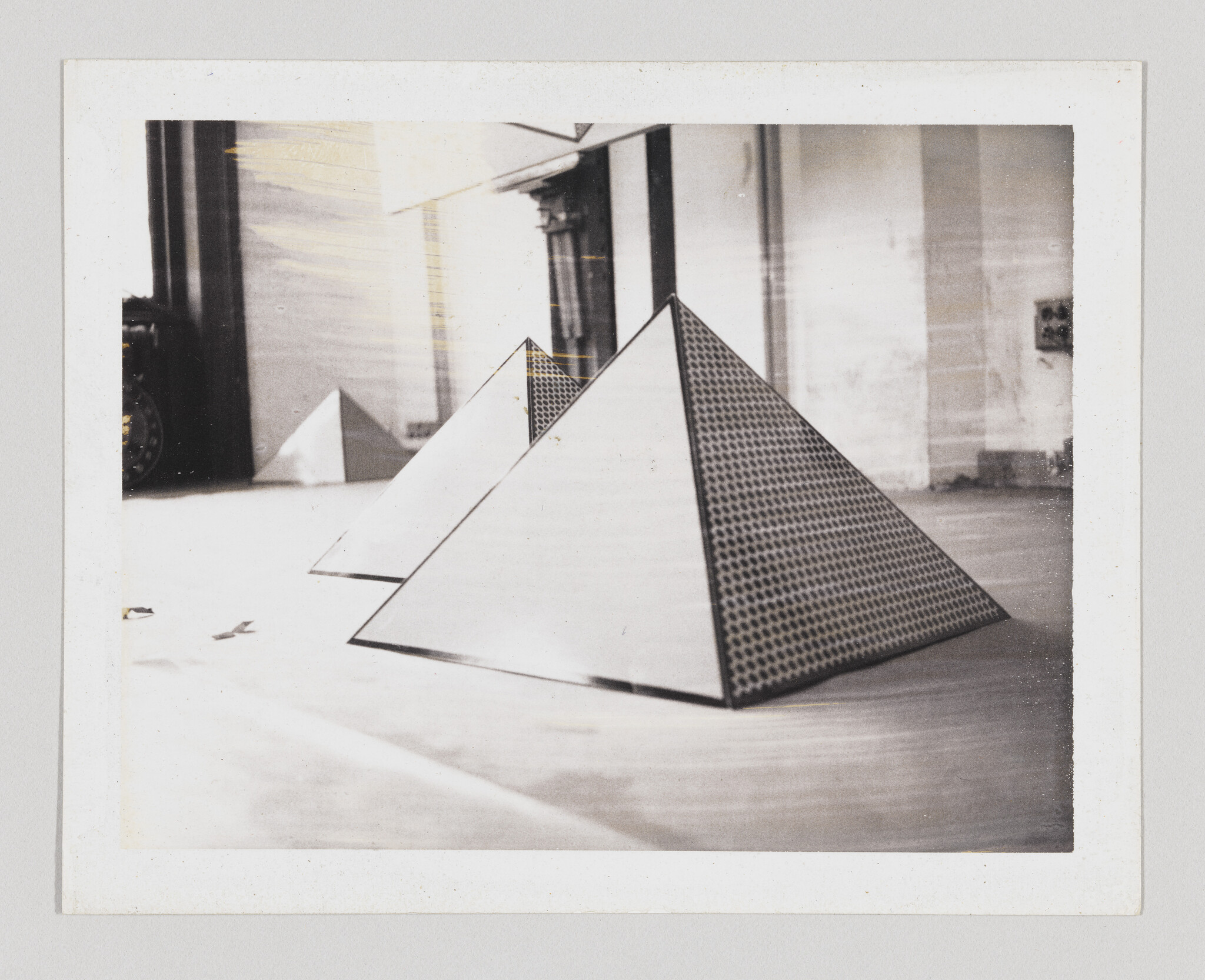 Three reflective pyramids with patterned surfaces are arranged on a floor in a bright room.