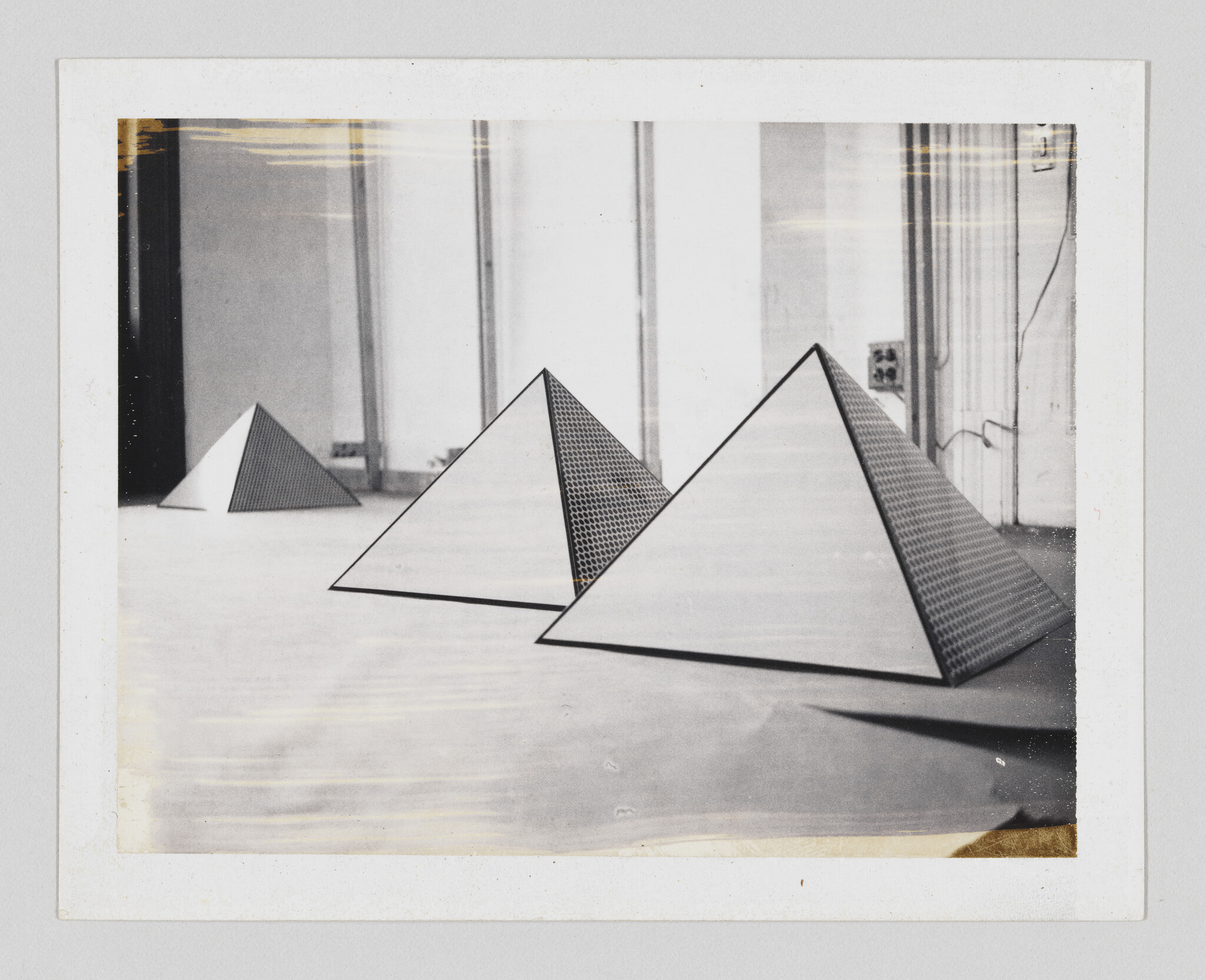 Three triangular pyramid sculptures with patterned sides arranged on a gallery floor.