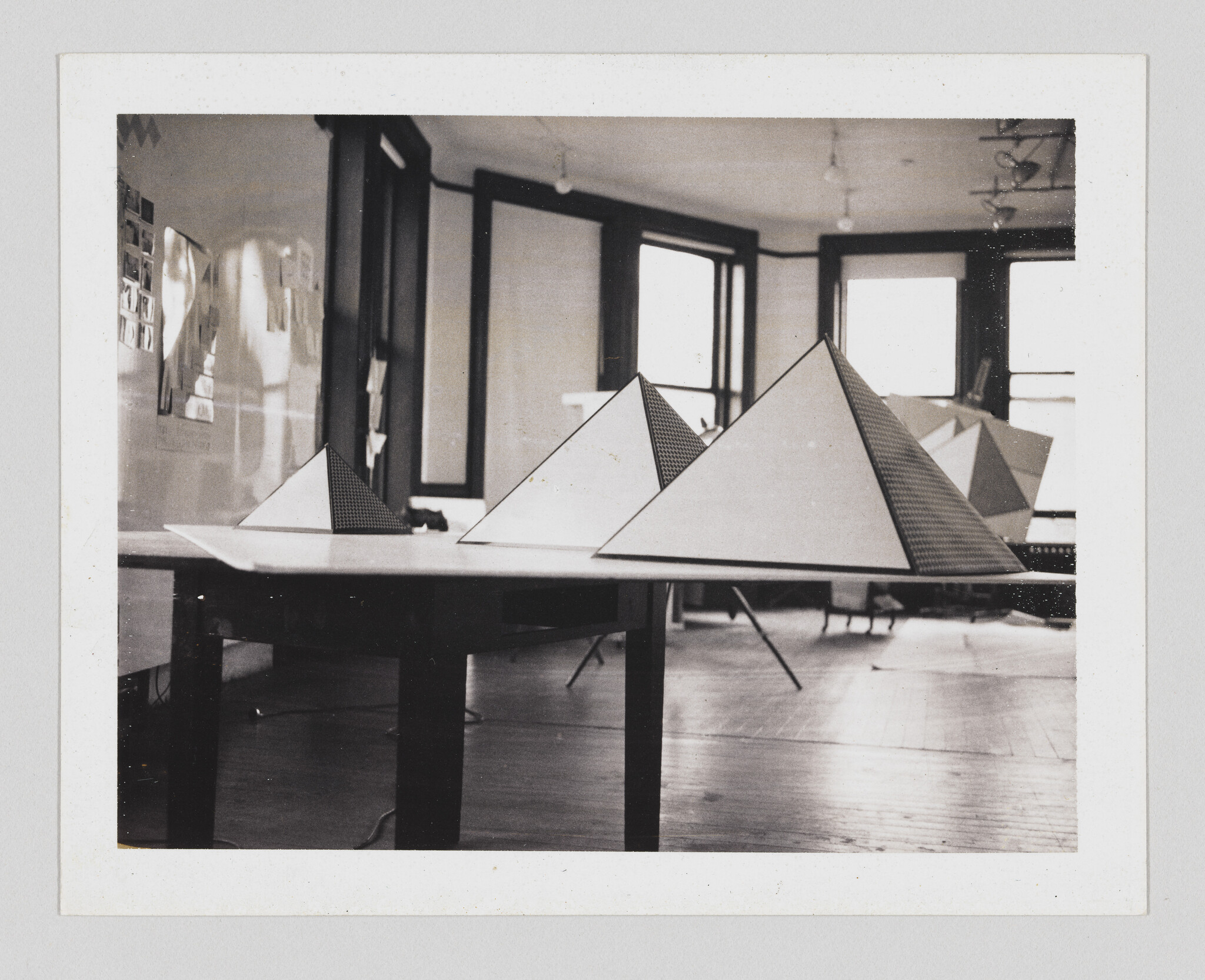 Three triangular pyramid models sit on a table in a bright design studio with large windows.