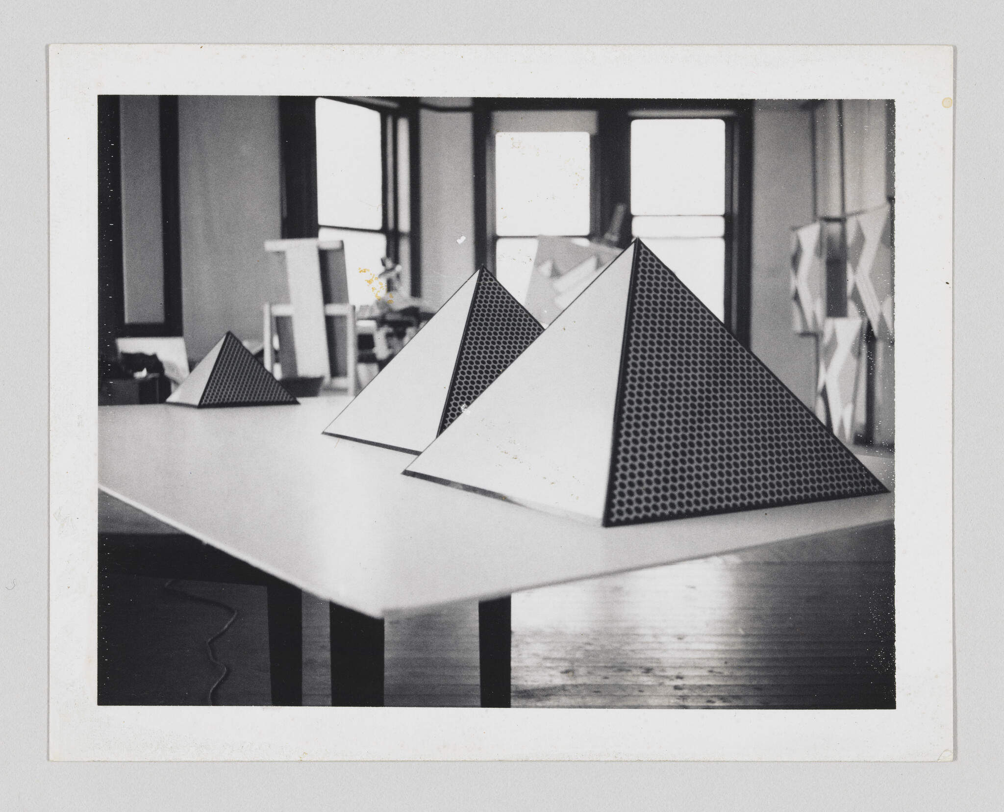 Three pyramid-shaped models with perforated sides sit on a table in an art studio.
