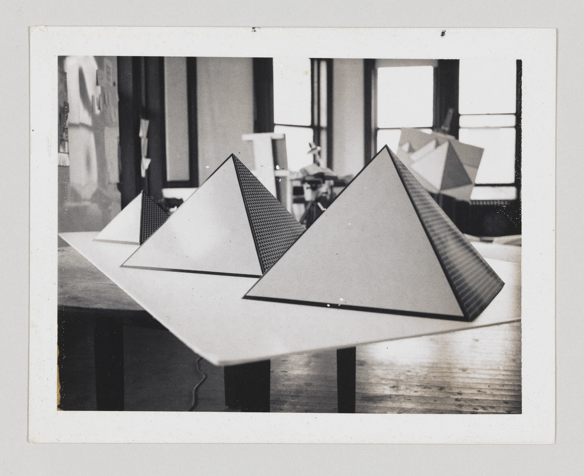 Three large paper pyramids sit on a table in a sunlit studio workspace.