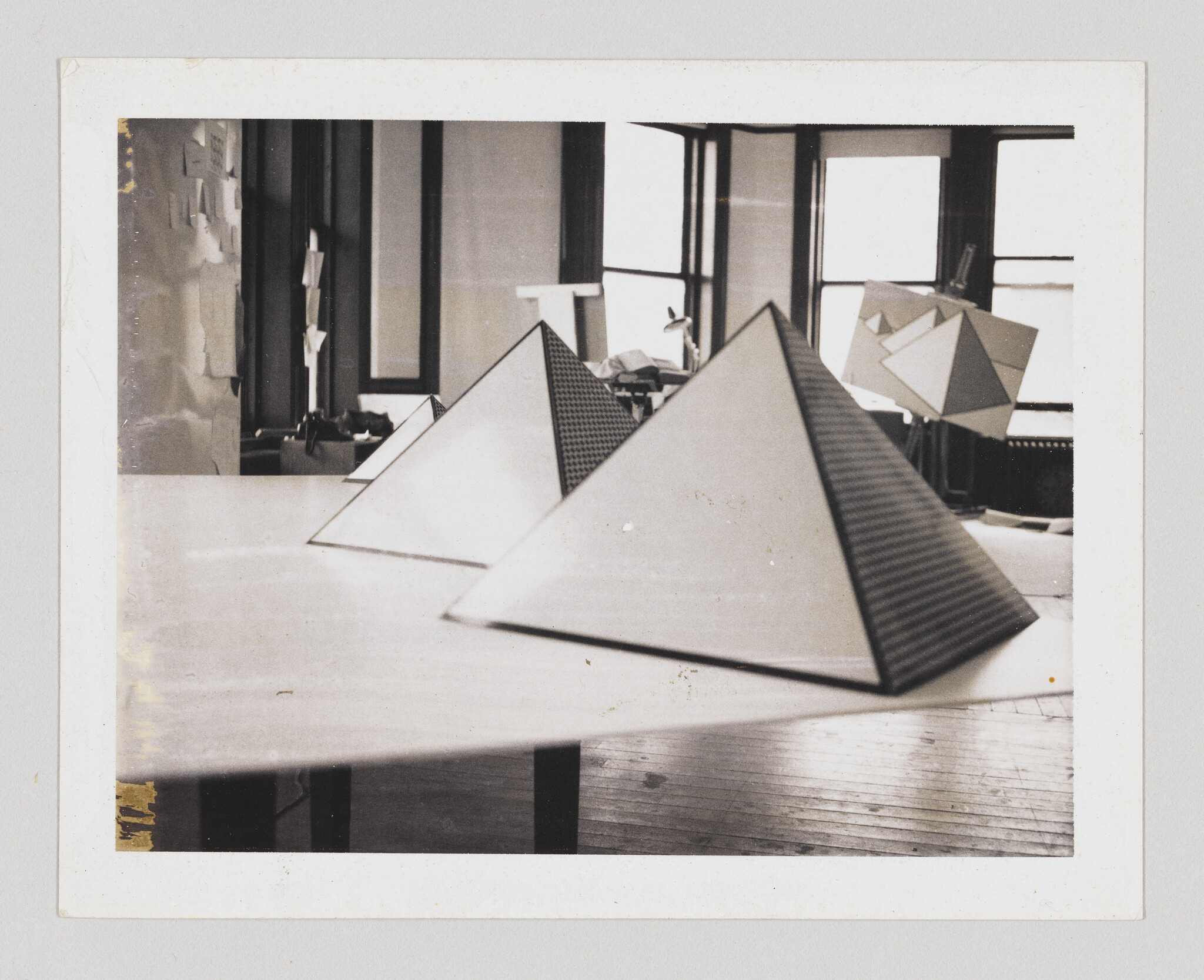 Three geometric pyramid models sit on a long table in an art studio near windows.