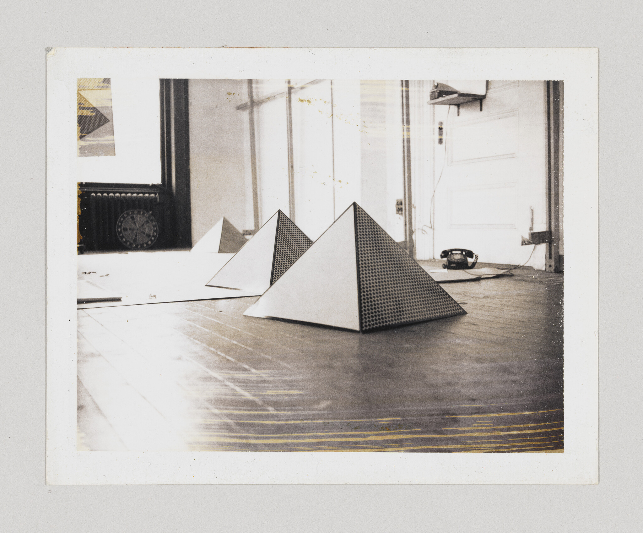 Three small pyramid-shaped sculptures with perforated sides sit on a wooden floor near a telephone.