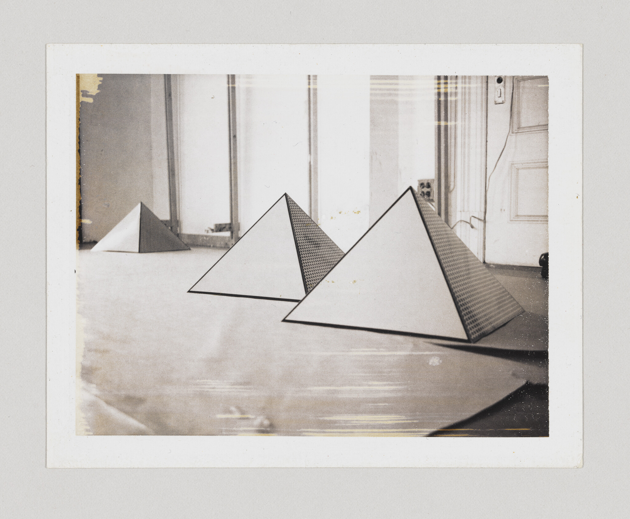 Three white triangular pyramids with patterned sides sit on a floor in an empty room.