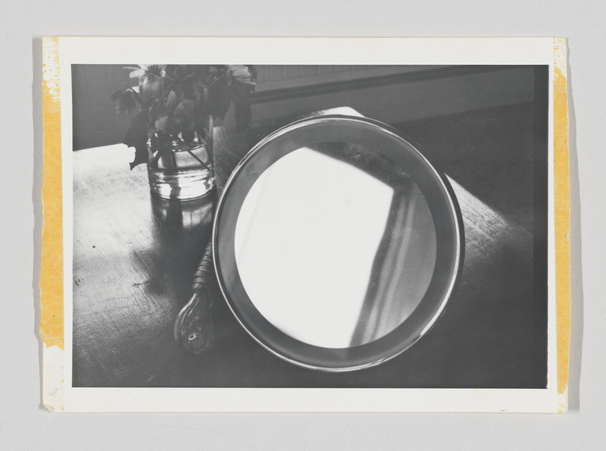 A round handheld mirror lies on a wooden table reflecting a bright window light.