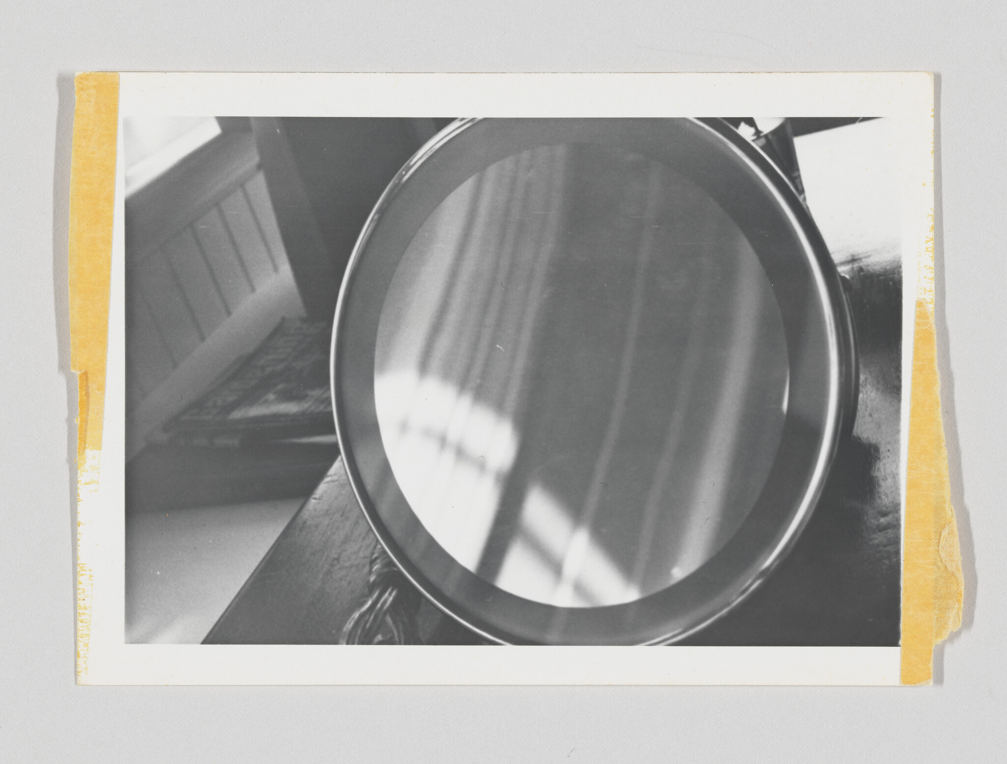 Round tabletop mirror reflects window panes and light while resting on a wooden surface.